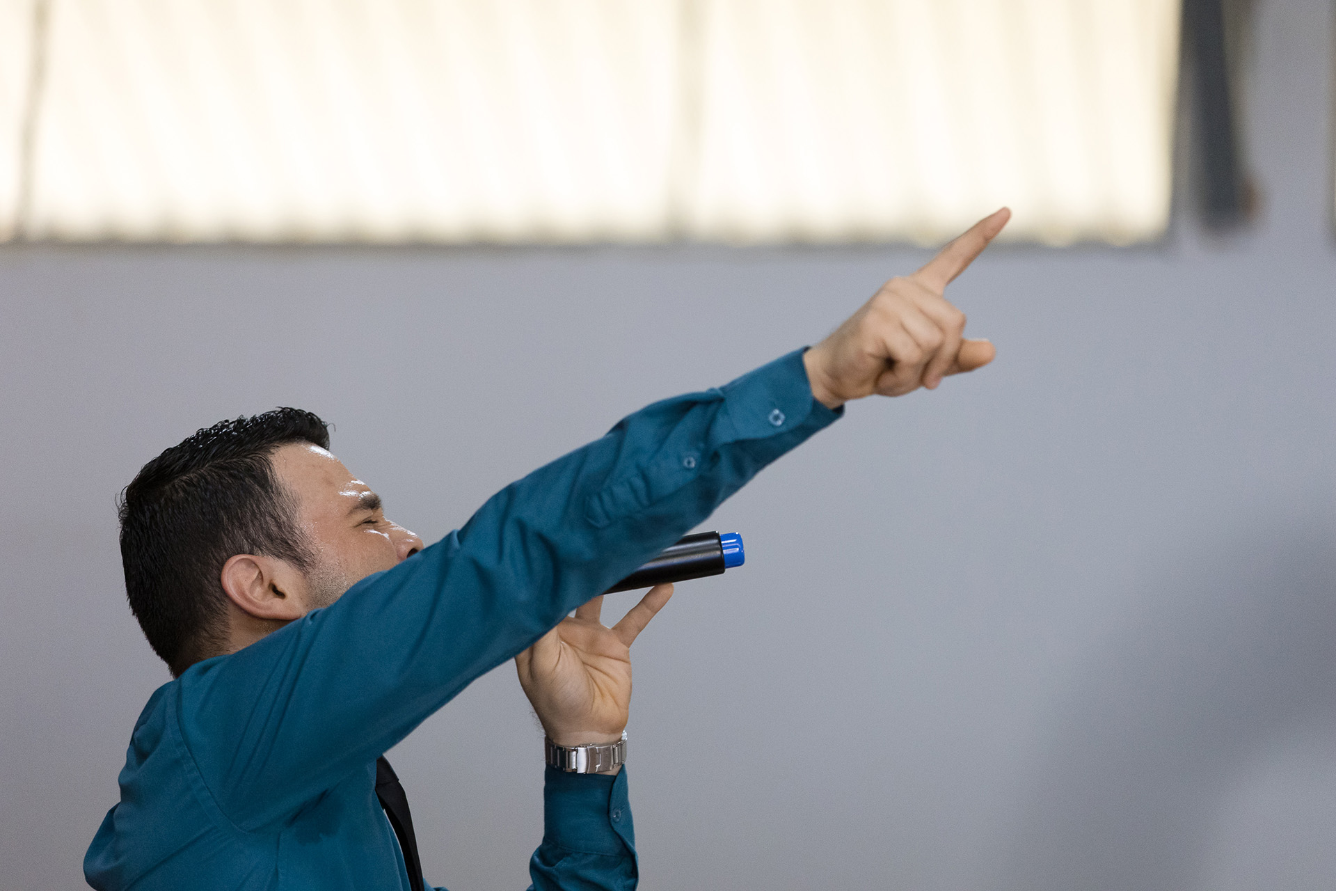 man in a local church holding a microphone with one hand and pointing with the other